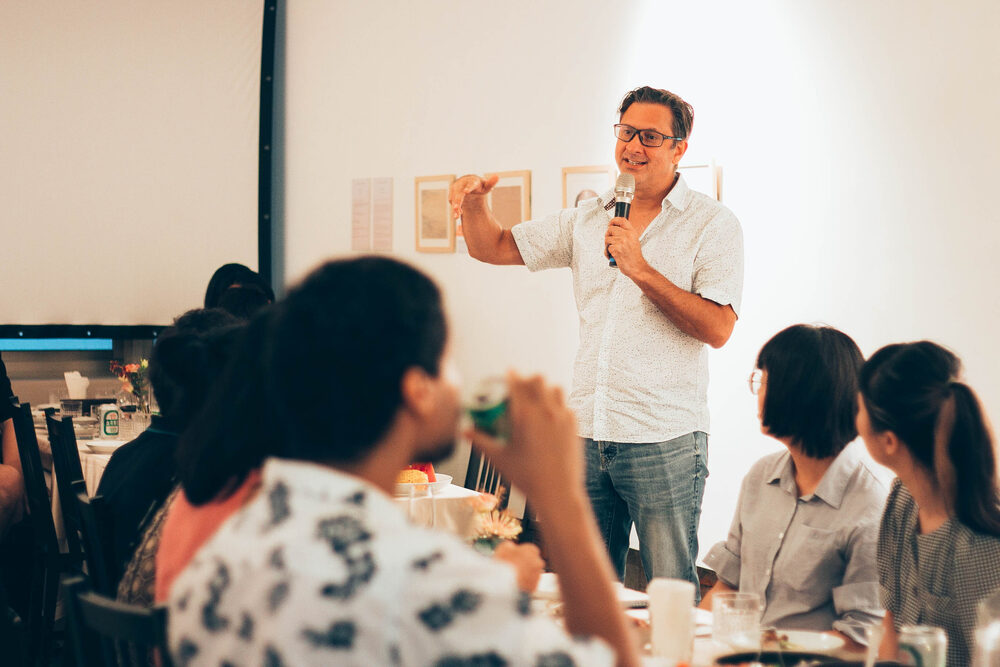 An artist speaking to seated guests in front of a hung wall of works